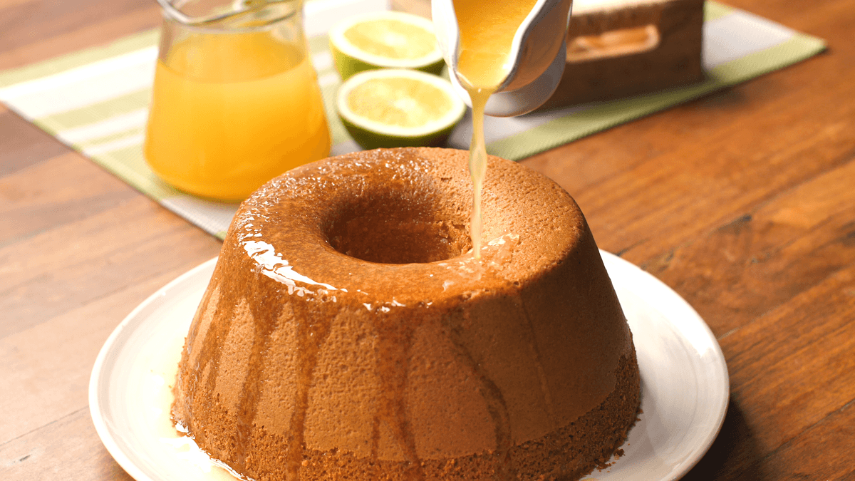 Bolo de laranja dourado com furo central regado com calda brilhante em prato elegante