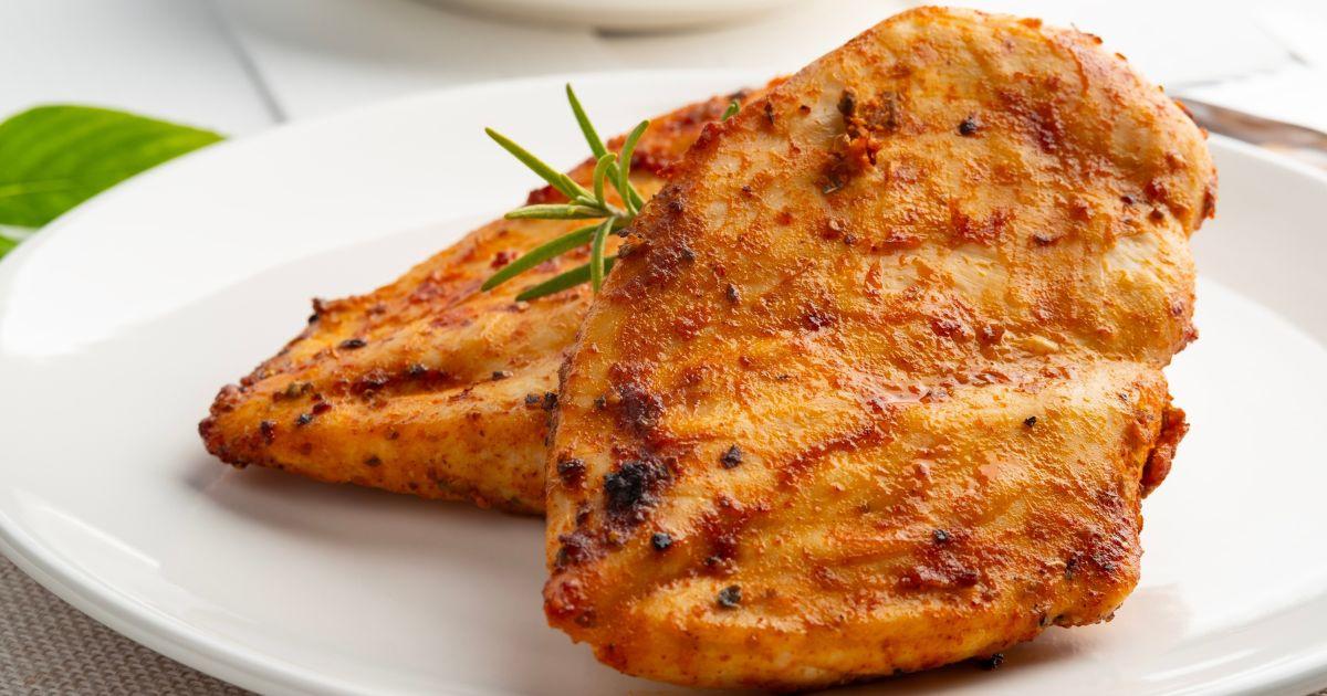 Cubos de peito de frango dourados e brilhantes com ervas frescas em prato moderno