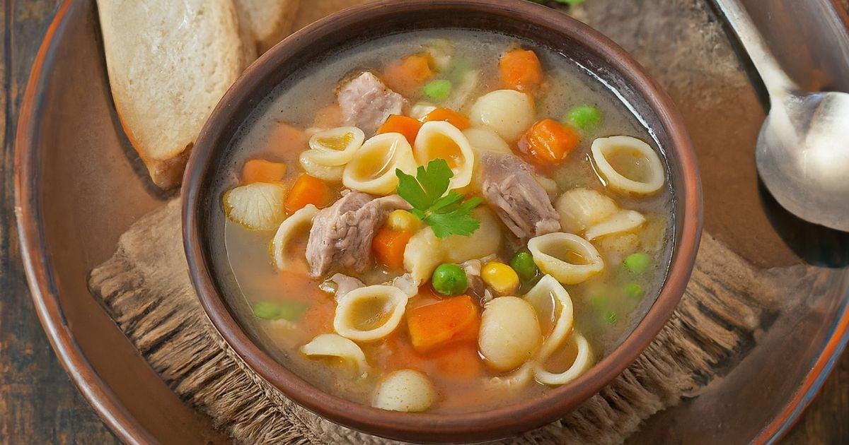 Prato fundo fumegante de sopa caseira de legumes com pedacinhos de carne, macarrão e cheiro-verde